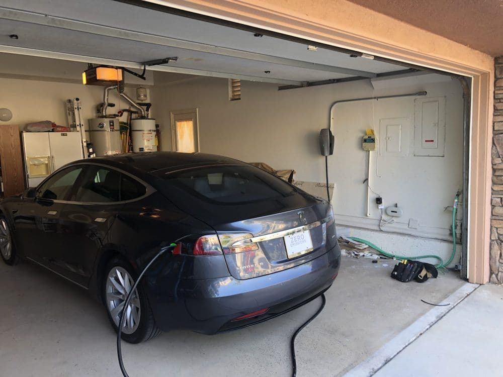 Tesla Model S charging in a modern garage with tools and appliances visible.