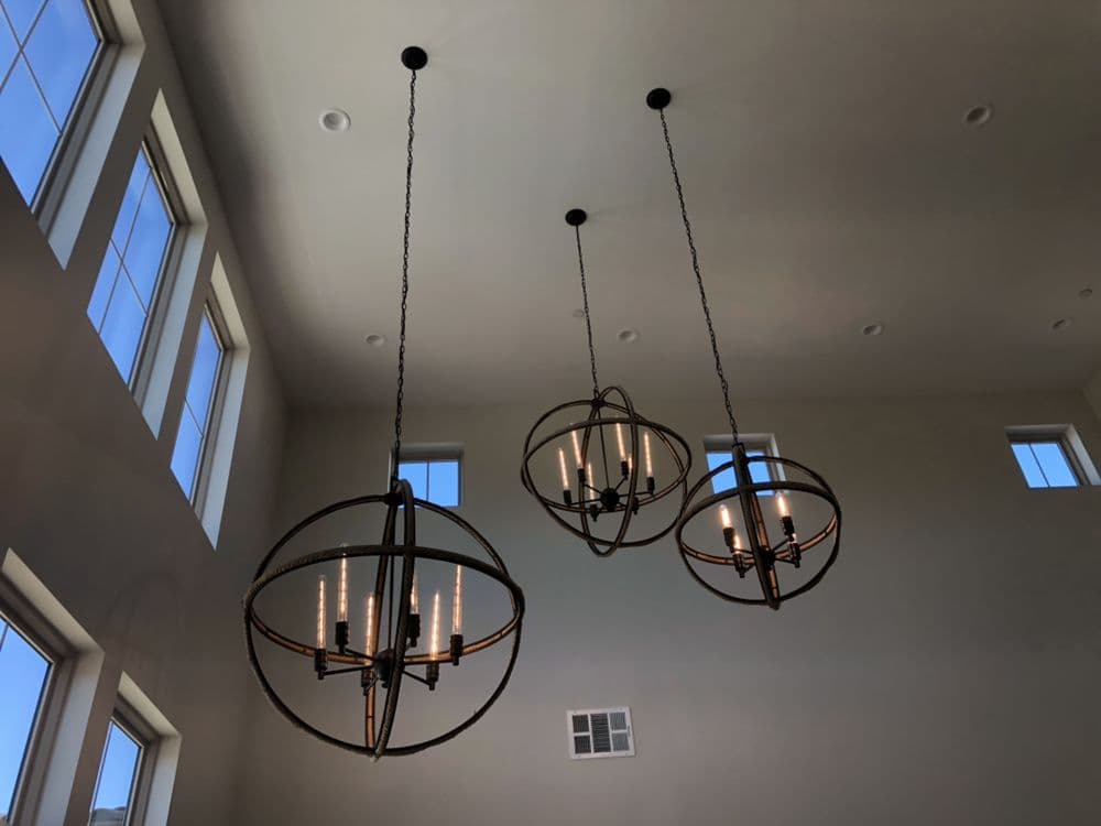 Modern chandeliers suspended from a high ceiling in a bright, airy room with large windows.