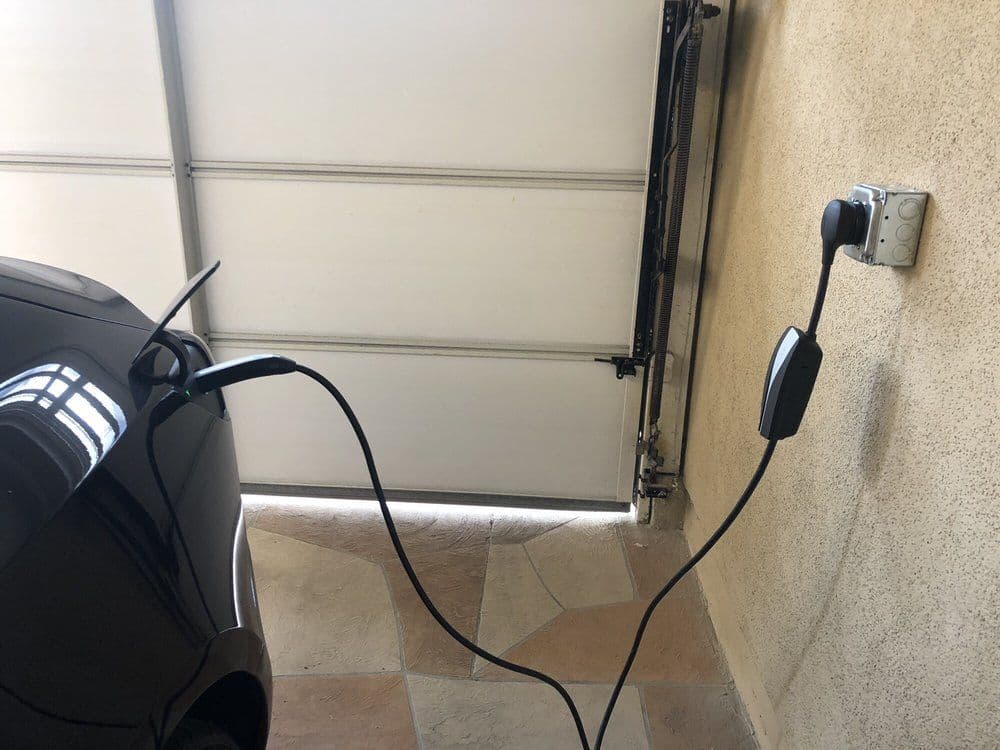 Electric car charging at home in garage, with charger plugged into wall outlet.
