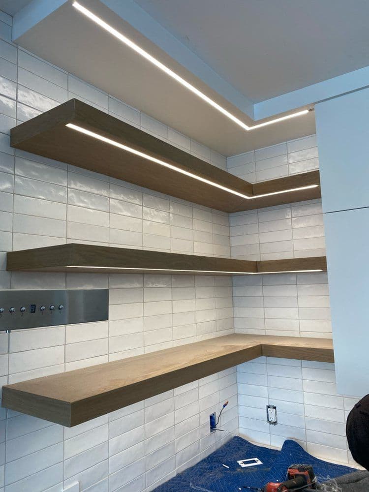 Modern wooden floating shelves with LED lighting on a tiled kitchen wall.