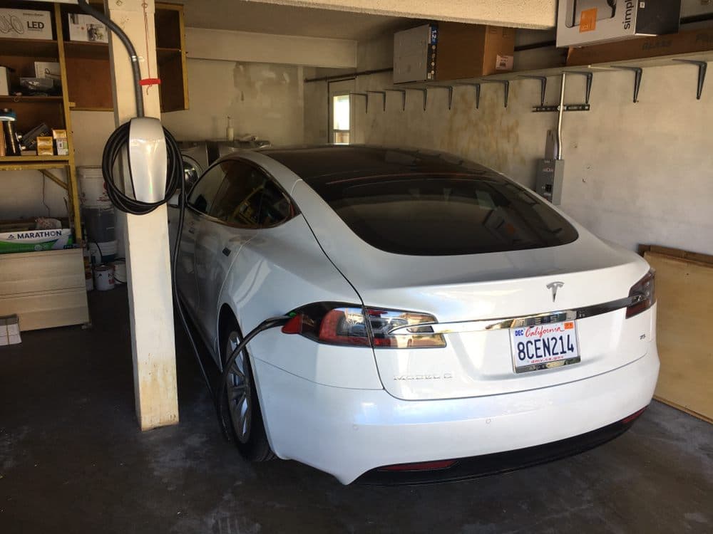 White Tesla Model S charging in a garage with charging station and storage background.