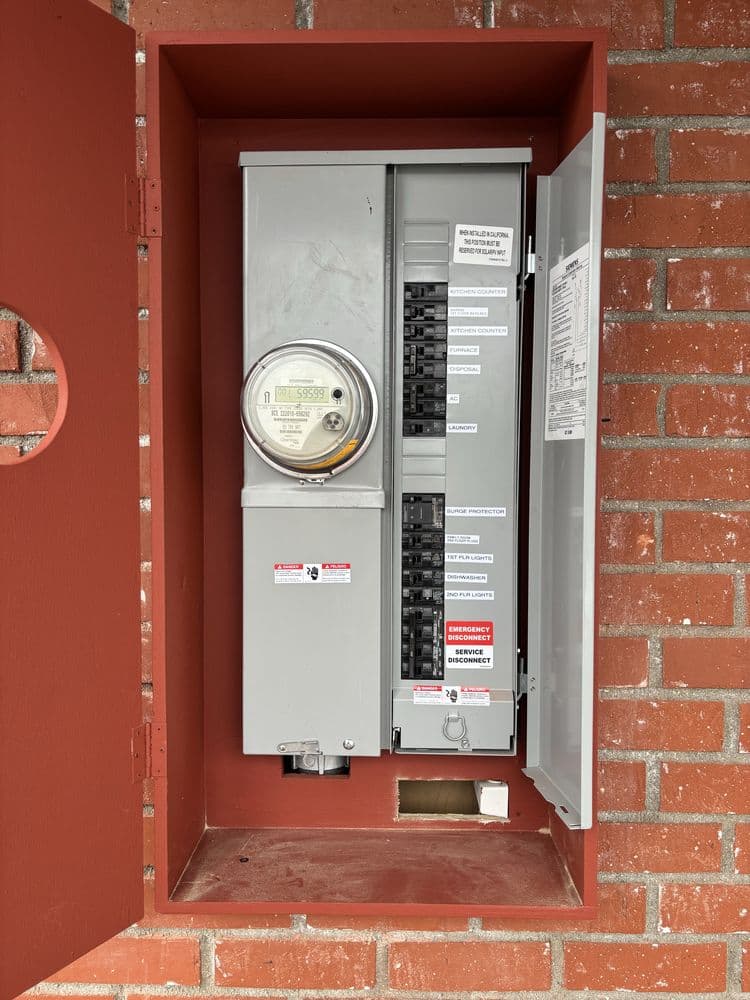 Electrical meter and circuit breaker panel mounted on red brick wall.