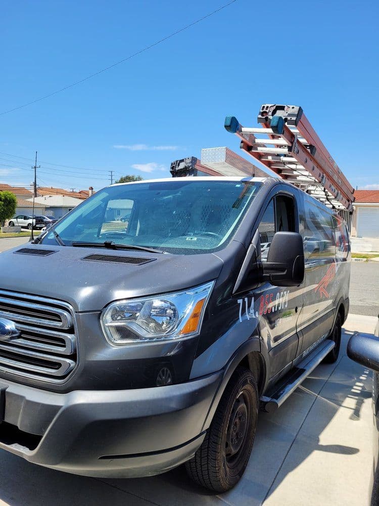 Gray utility van with ladder on roof parked in residential area under clear blue sky.