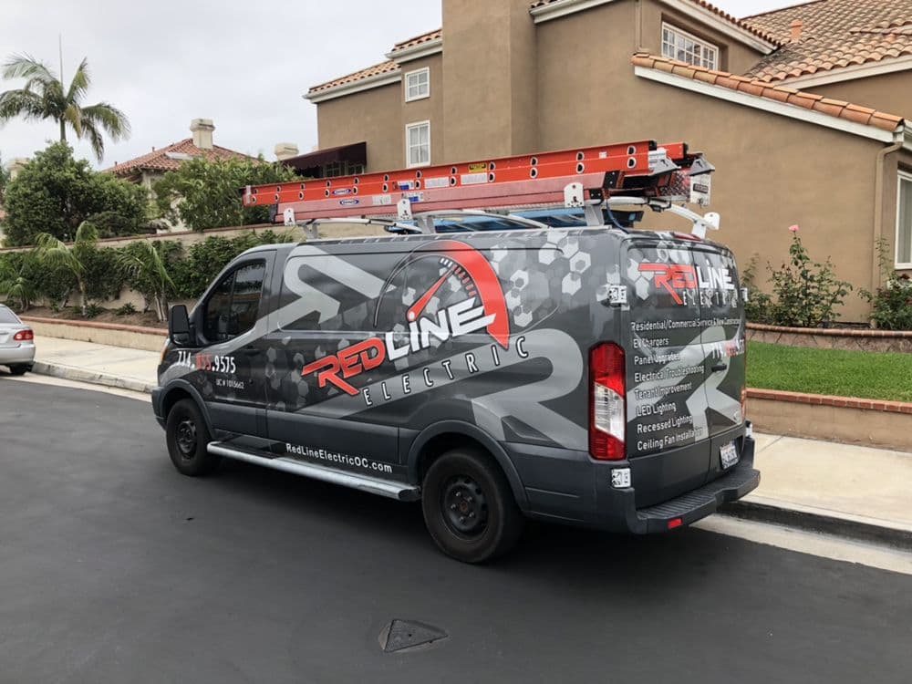Red Line Electric service van parked in residential area with ladders on top.