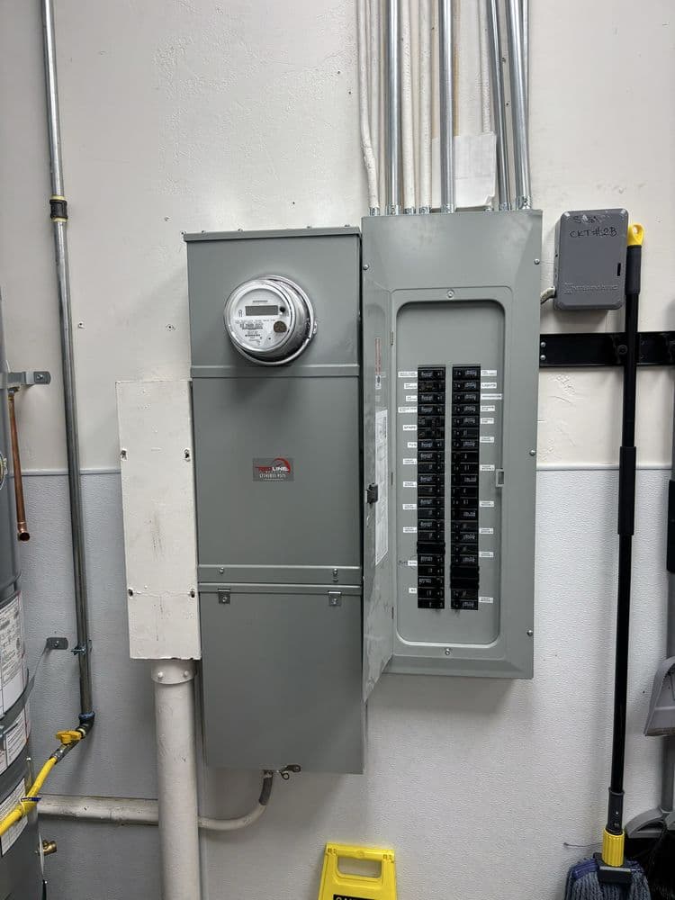Electrical panel with circuit breakers and smart meter in a utility room setting.