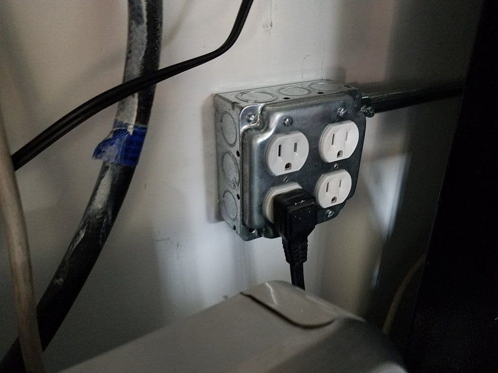 Electrical outlet box with three outlets and power cord connected, mounted on a wall.