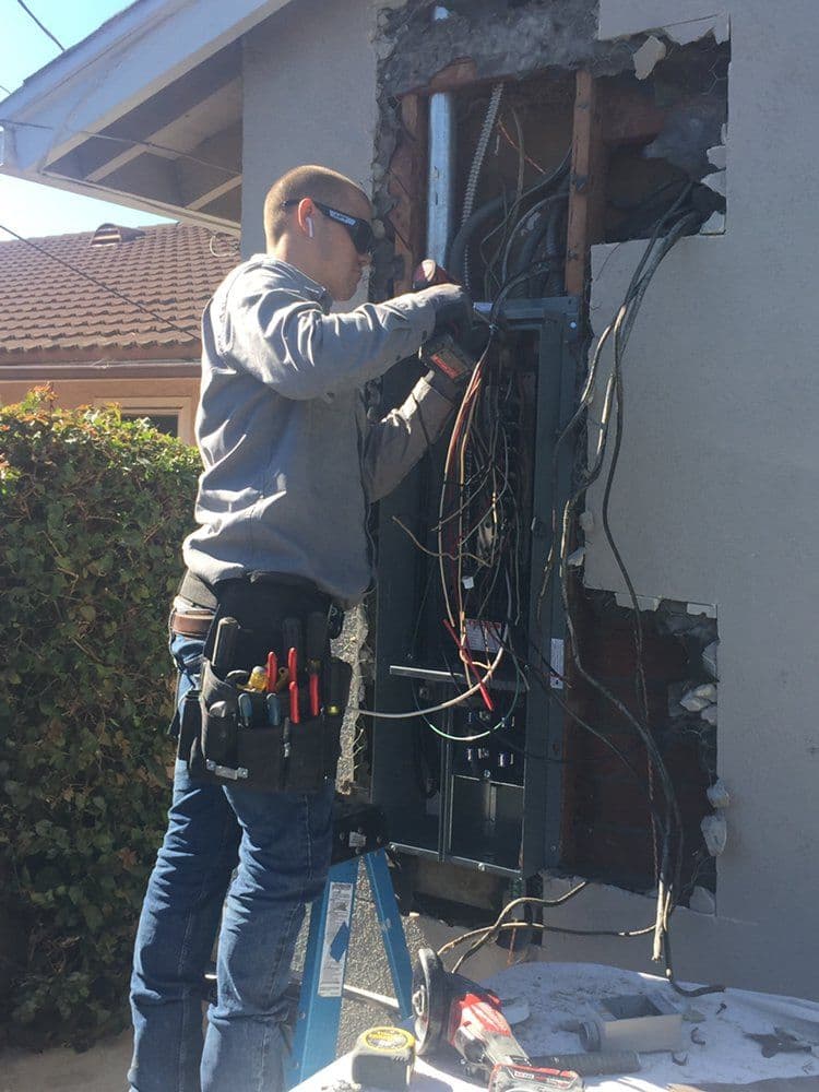 Electrician working on electrical panel installation, surrounded by wires and tools.