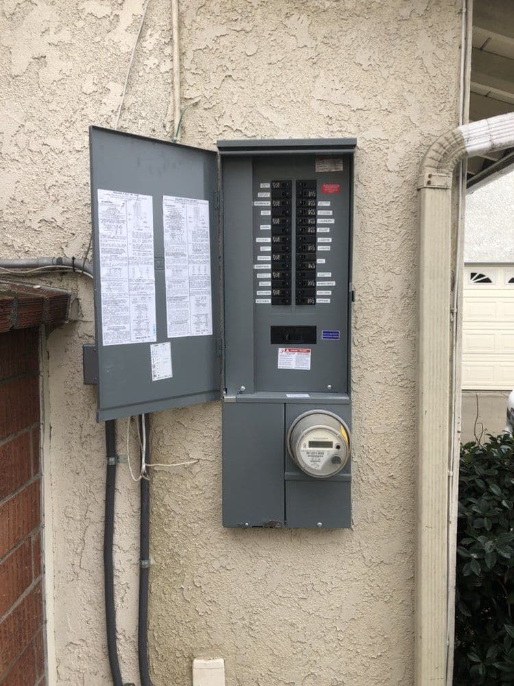 Electrical panel with circuit breakers and meter on an exterior wall of a home.