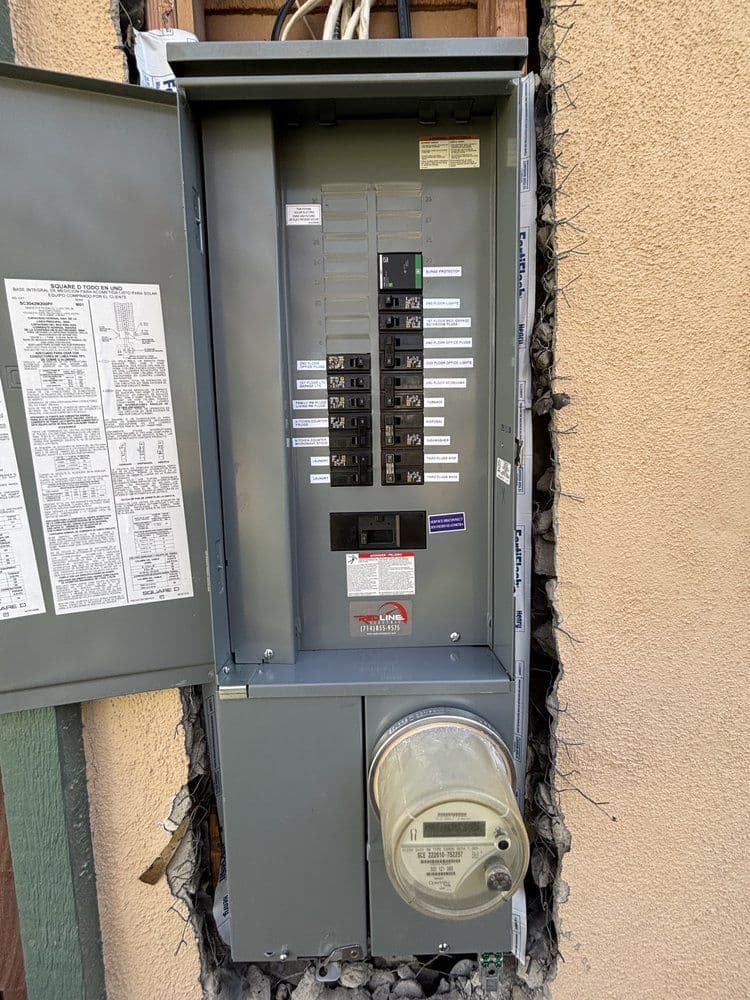 Electric panel with circuit breakers and meter, mounted on an exterior wall.