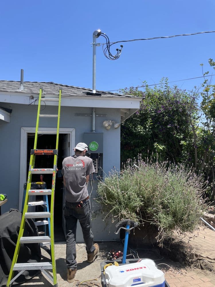 Technician installing equipment on a house roof with a ladder and tools in the background.