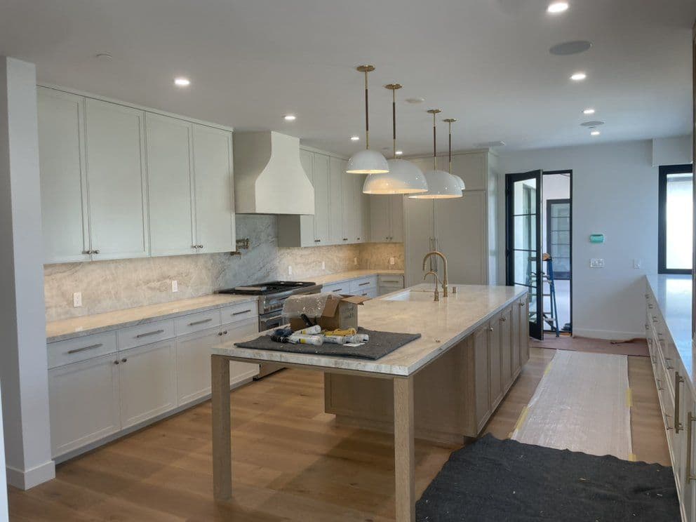 Modern kitchen with white cabinets, marble countertops, gold pendant lights, and a large island.