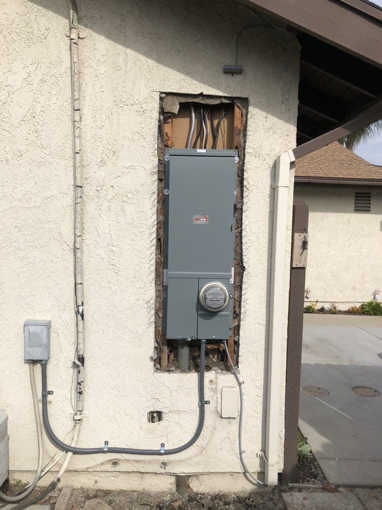 Electric service panel and meter installed outside a home with exposed wiring.