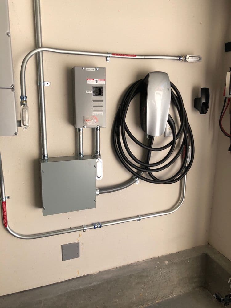 Electric vehicle charging station installed on garage wall with cables and electrical panel.