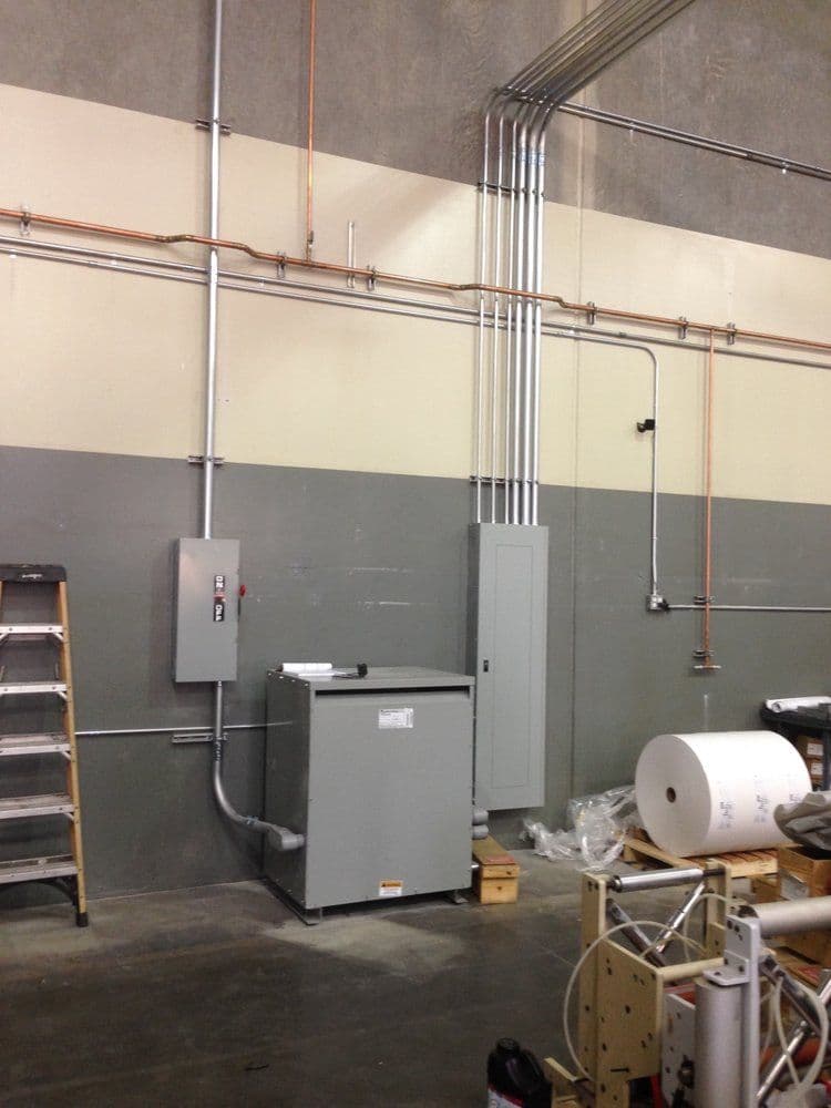 Industrial electrical setup with panels, pipes, and equipment in a warehouse environment.