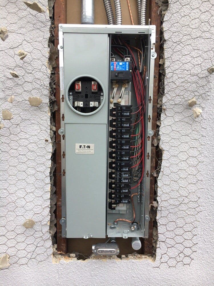 Electrical panel installation in a wall with exposed wiring and circuit breakers.
