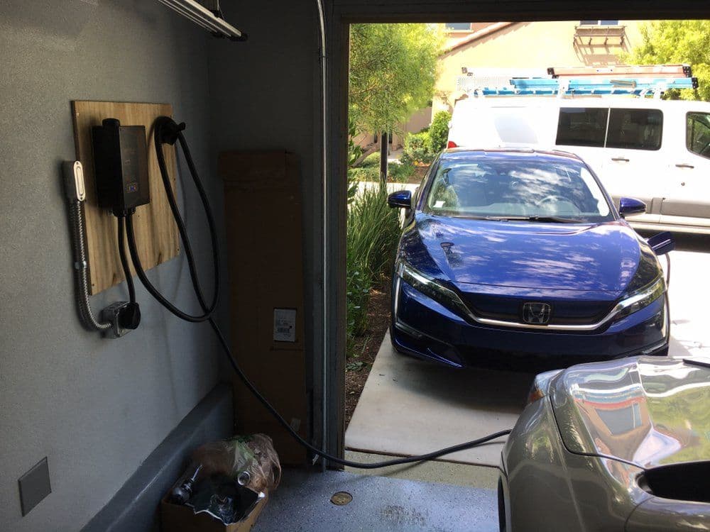 Electric vehicle charging station in a garage with a blue Honda car parked inside.