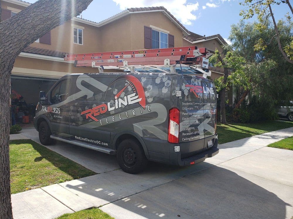 Red Line Electric van parked in residential driveway with ladder on top, sunny day.