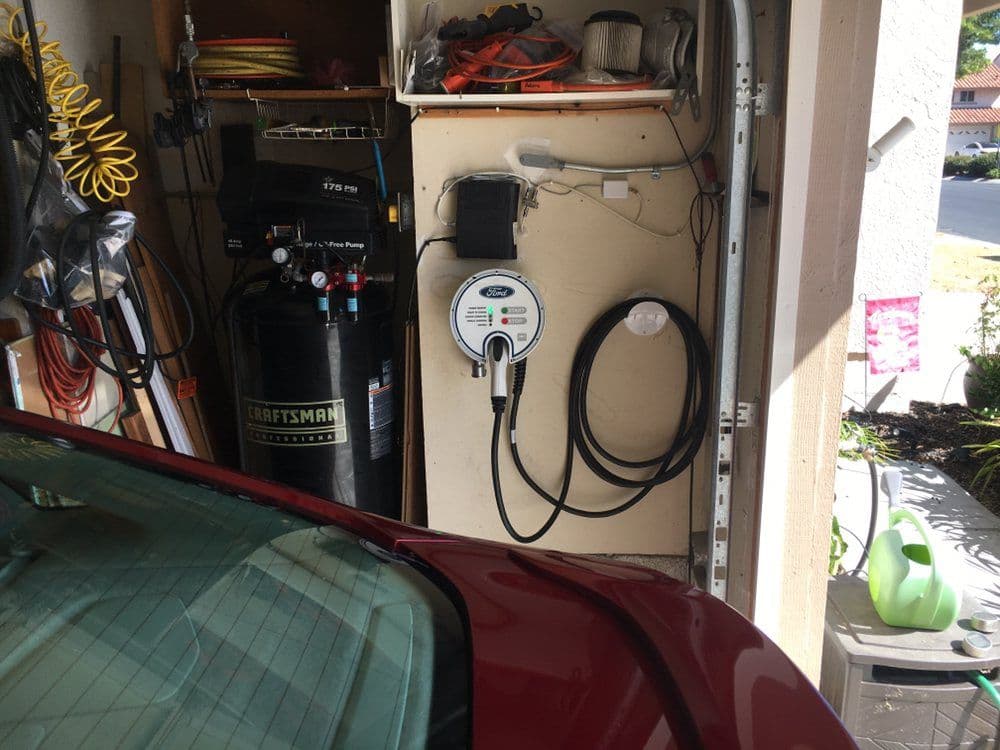 Electric vehicle charger mounted on a garage wall next to tools and equipment.