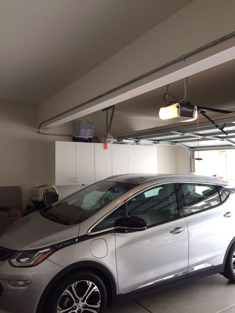Silver electric car parked in a spacious garage with organized storage and overhead lighting.