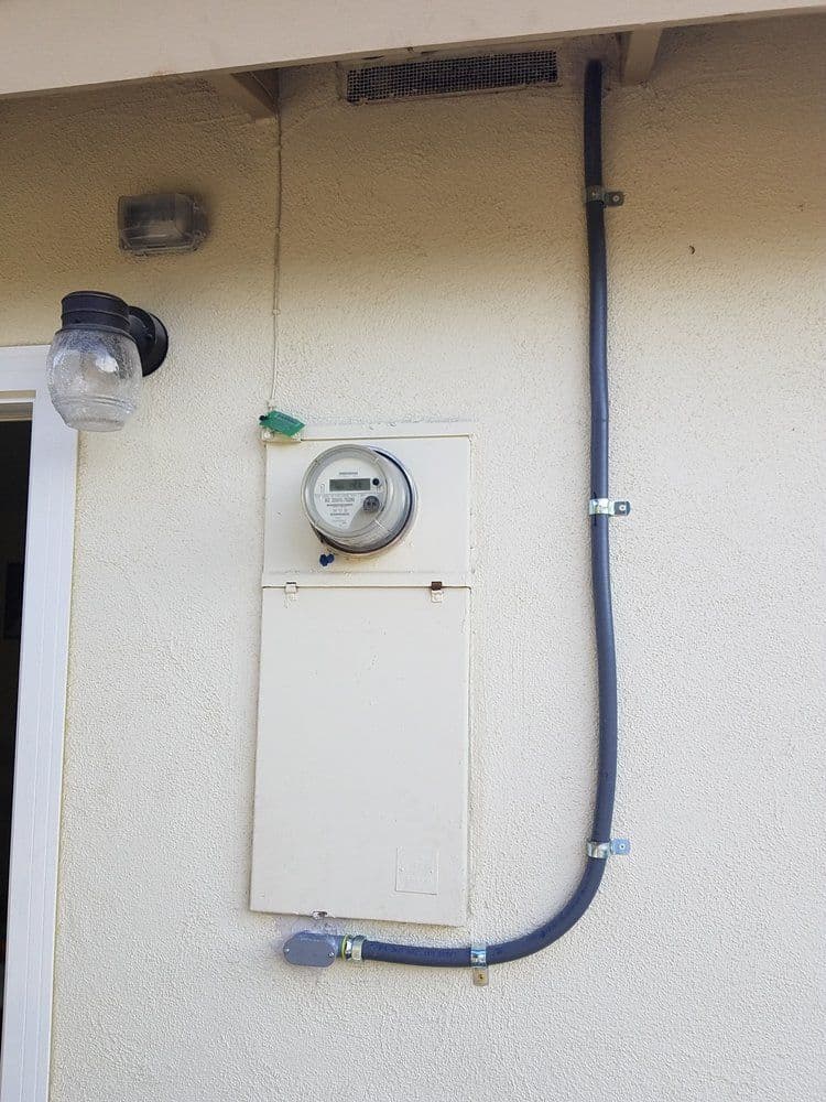 Electric meter mounted on wall with conduit and utility box above a porch light.