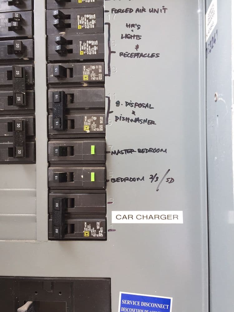 Electrical panel with labeled circuit breakers for home appliances and car charger.