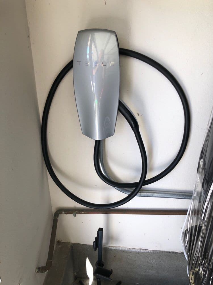Tesla wall charger mounted in a garage, featuring a sleek design and coiled charging cable.
